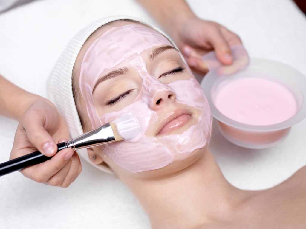 Young beautiful girl receiving pink facial mask in spa beauty salon - indoors